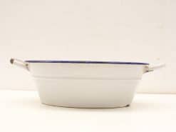 Vintage white enamel dish with blue rim and handles, perfect for serving and baking.