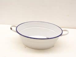 Vintage oval white enamel pot with navy rim, showcasing charming signs of use and history.