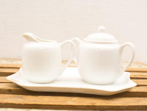 Elegant white porcelain tea set with cream jug and sugar bowl on curved tray.