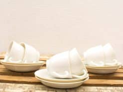 Elegant white ceramic cups and saucers on rustic wood, perfect for cozy gatherings.