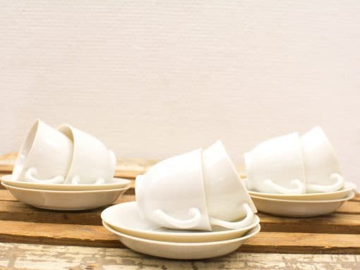 Elegant white ceramic cups and saucers on rustic wood, perfect for cozy gatherings.