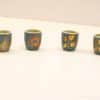 Set of 4 teal ceramic cups with vibrant botanical designs in orange and gold.