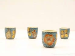 Vibrant vintage ceramic cups with floral designs in blue, orange, and purple accents.