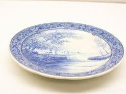Elegant blue and white porcelain plate featuring a serene riverside landscape and floral motifs.