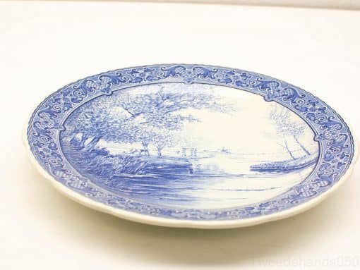 Elegant blue and white porcelain plate featuring a serene riverside landscape and floral motifs.