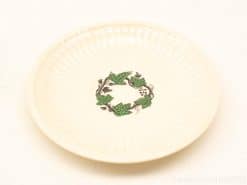 Elegant cream plate with green leaves and dark berries, perfect for decoration or dining.