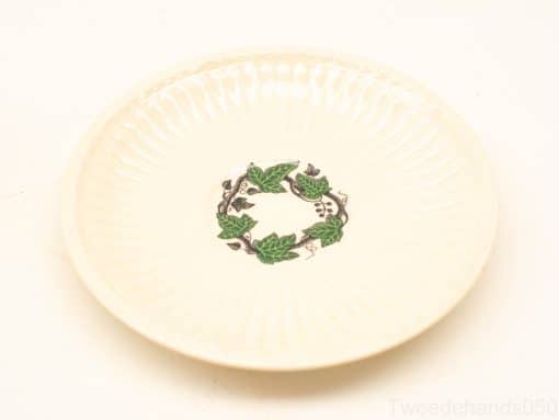 Elegant cream plate with green leaves and dark berries, perfect for decoration or dining.