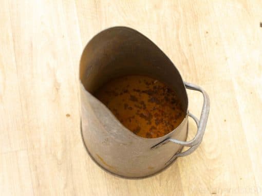 Vintage metal bucket with murky brown liquid; shows signs of wear and rust.