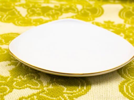 Elegant triangular white porcelain plate with gold rim for sophisticated dining presentations.