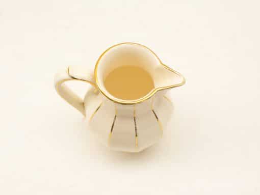 Elegant cream ceramic pitcher with golden accents, perfect for serving beverages stylishly.