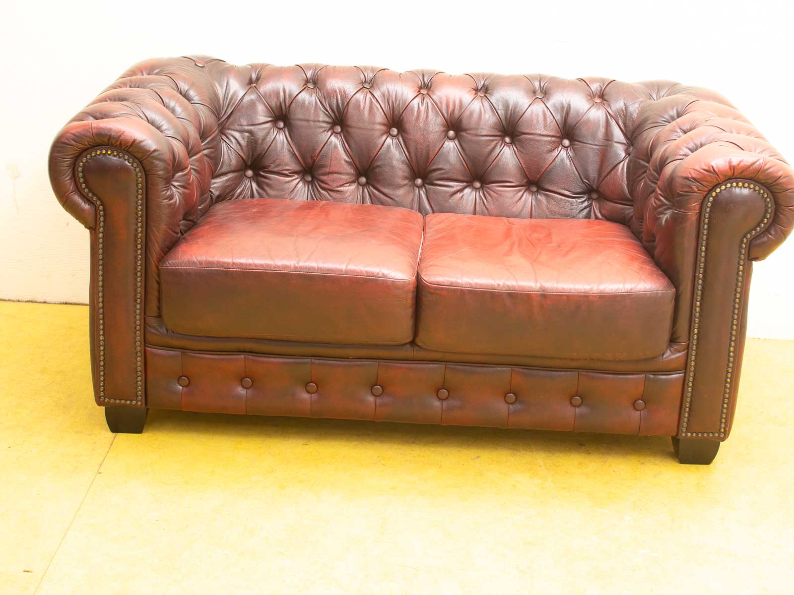 Elegant burgundy Chesterfield sofa with deep-button tufting and brass nailhead trim for timeless style.