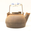 Antique kettle with rustic charm and blue floral handle, perfect for vintage decor enthusiasts.