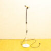 Sleek microphone on white stand against light wall and vibrant yellow floor. Ideal for audio use.