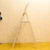 Used white ladder in a functional workspace with cream wall and vibrant yellow floor.