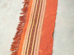 Handwoven terracotta textile with geometric patterns and playful fringes for artistic home decor.