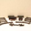 Vintage toy train set with black steam locomotive and green passenger car on weathered metal tracks.