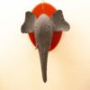 Handcrafted black elephant head wall sculpture with vivid reddish-orange mount against a neutral background.