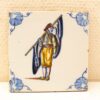 Hand-painted traditional tile featuring a colorful folkloric figure and intricate blue motifs.