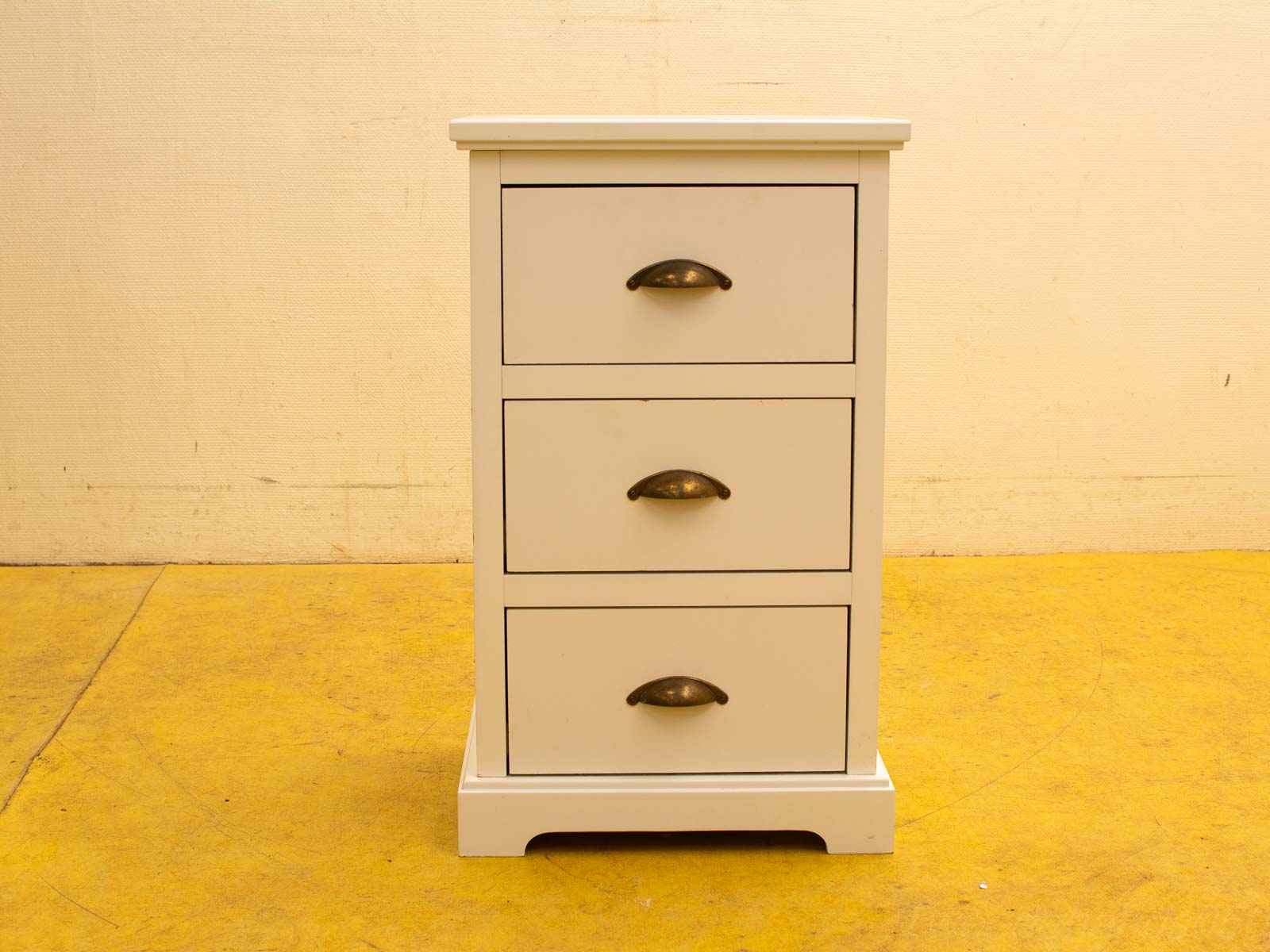 Stylish white nightstand with three drawers and bronze handles, perfect for modern interiors.