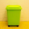 Heldergroene prullenbak met wielen op een gele vloer, ideaal voor recycling en afvalbeheer.