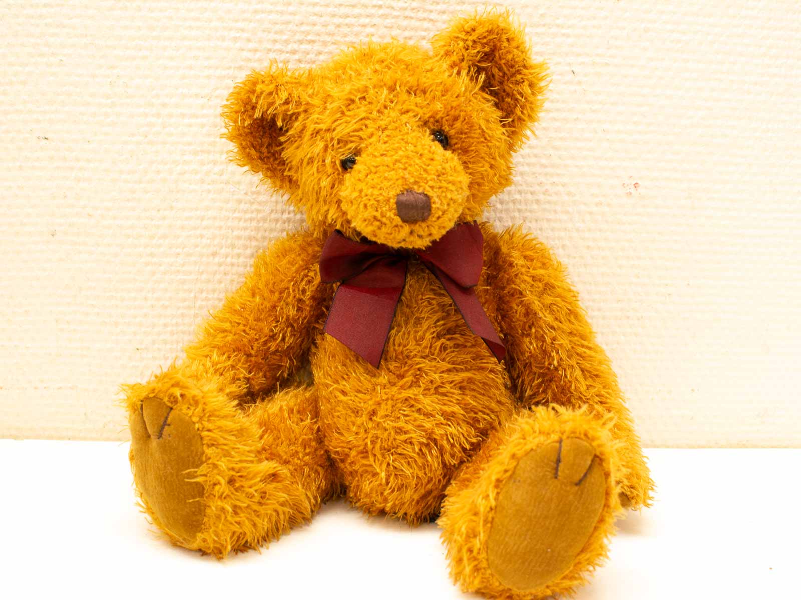 Charming golden-orange teddy bear with a burgundy bow, perfect for cuddles and nostalgia.