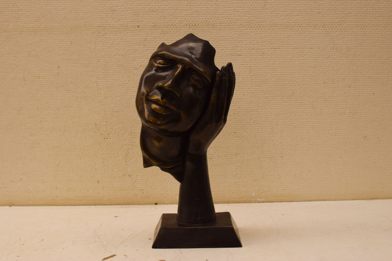 Bronzen beeld van een masker tegen een hand 48151